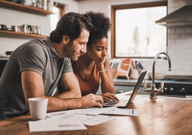 Couple in their kitchen doing financial planning on a laptop.