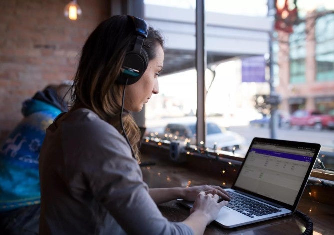 Woman working remotely on laptop at coffee shop counter.