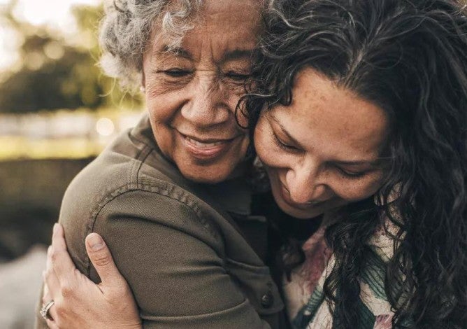 An older adult and her daughter smile and hug.