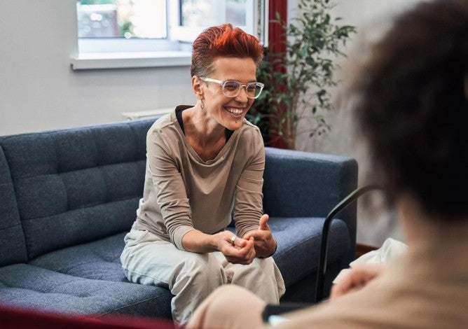 Woman laughing out loud while sitting at sofa and talking with her doctor during therapy.