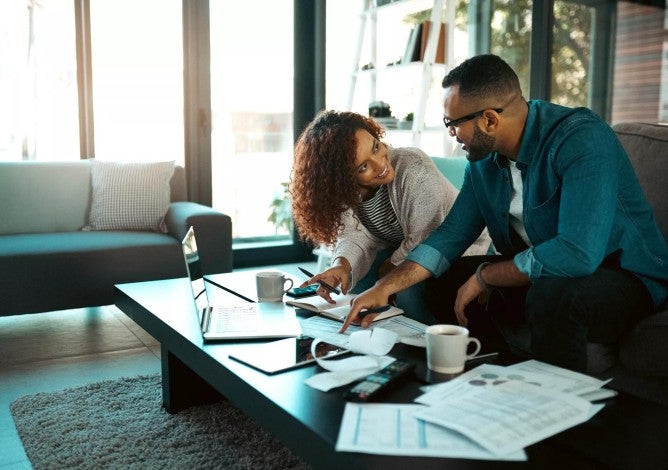 Black couple sitting together on a couch paying bills and reviewing finances