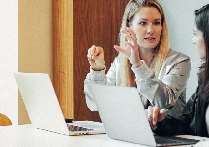 Dos mujeres revisando información sobre préstamos estudiantiles en computadoras.