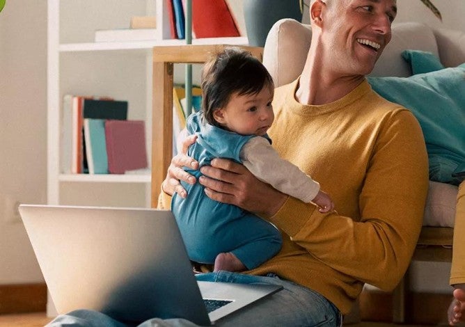 Father holding child and talking to another child while looking at budget on computer