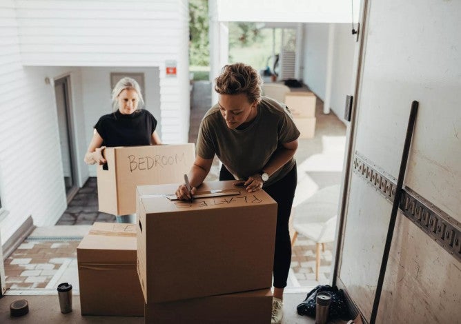 Woman holding box while female writing on cardboard box in moving van