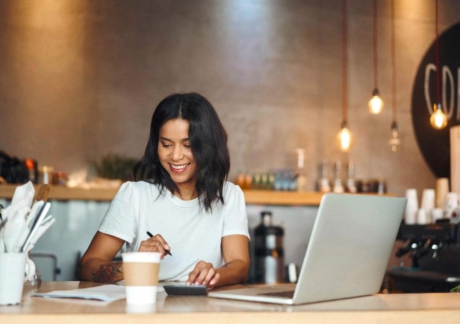 Business owner with coffee and a laptop, smiling as she works.