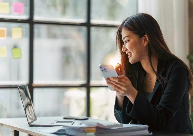 Young woman using her laptop and checking her phone.