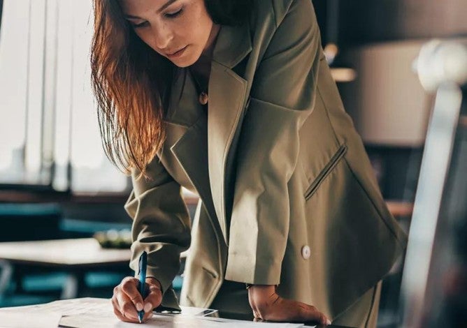 Photo of a woman leaning over a table and reviewing documents related to her investments due to market volatility.