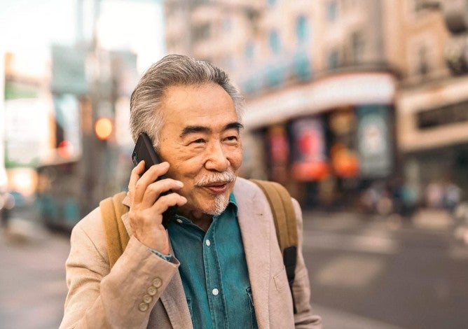 Middle age Asian man walking on the street, smiling, while talking on the phone