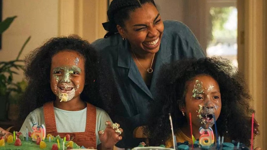 A mother smiling with her two daughters who have birthday cake on their faces