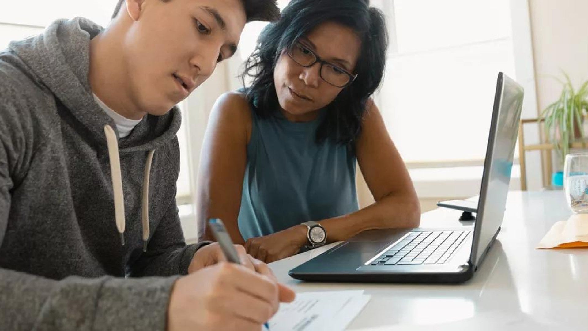 Photo of a mother and son sitting in front of a laptop and reviewing options for paying for college.
