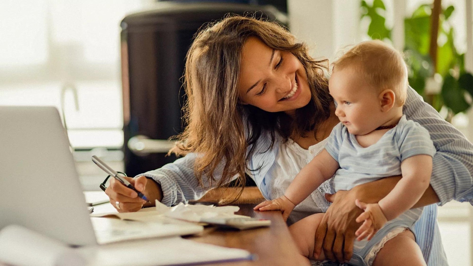 Photo of woman smiling at baby while she works on a laptop.