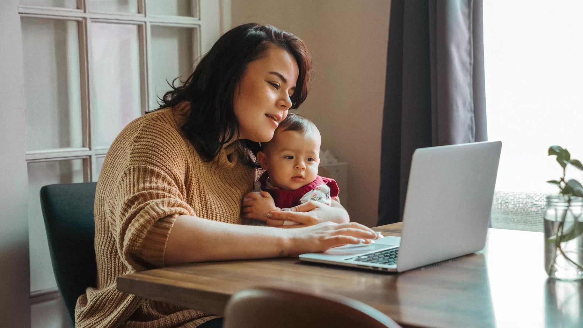 Mujer sosteniendo a un bebé en su regazo y mirando su puntaje crediticio en una computadora.