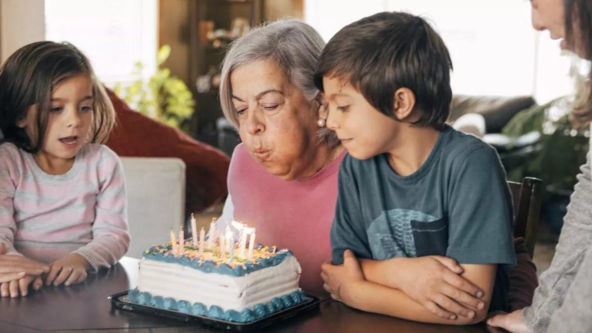 An older adult blowing out the candles on her birthday cake while her family watches.