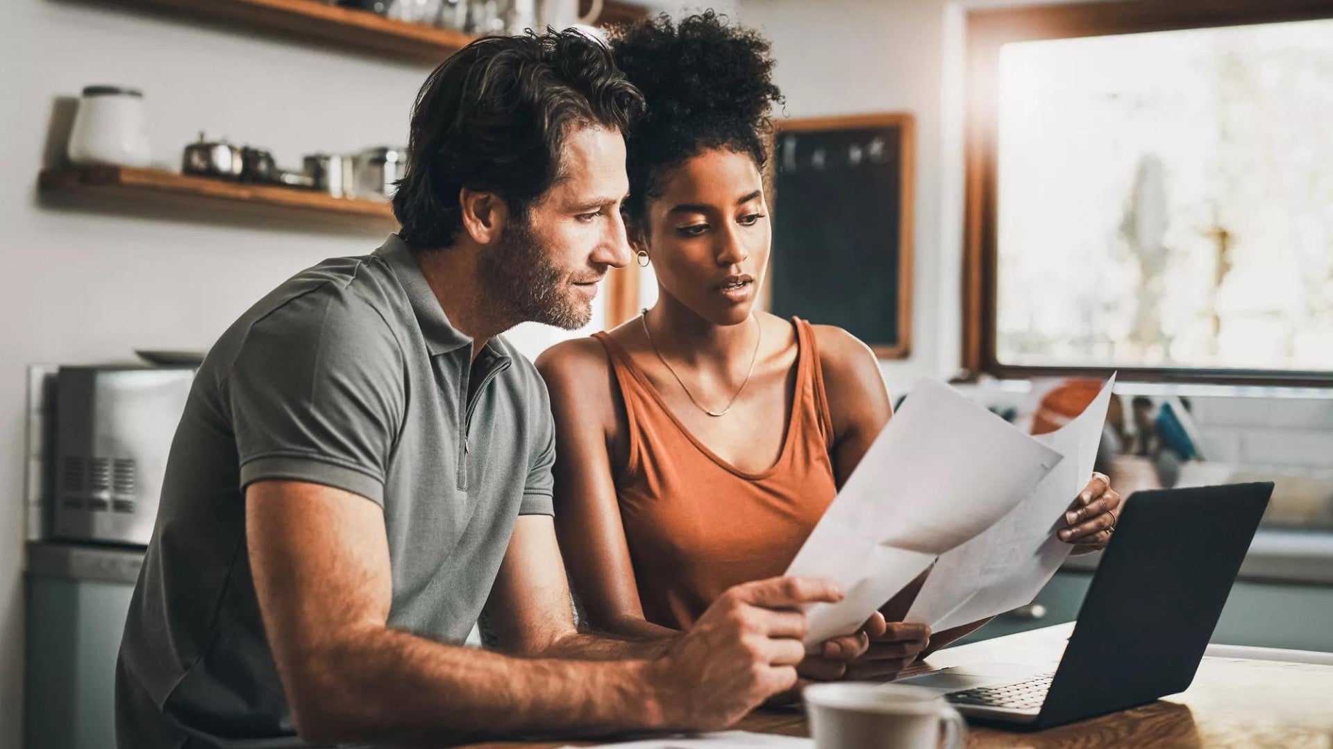 Man and woman seated at a kitchen table looking at retirement contributions on a laptop computer