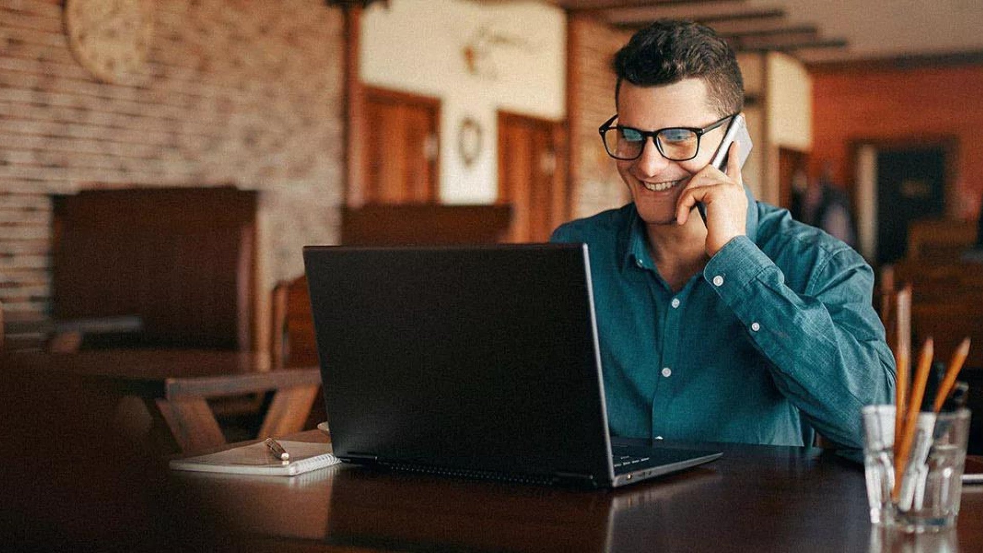 Photo of a man on a computer talking on his cell phone.