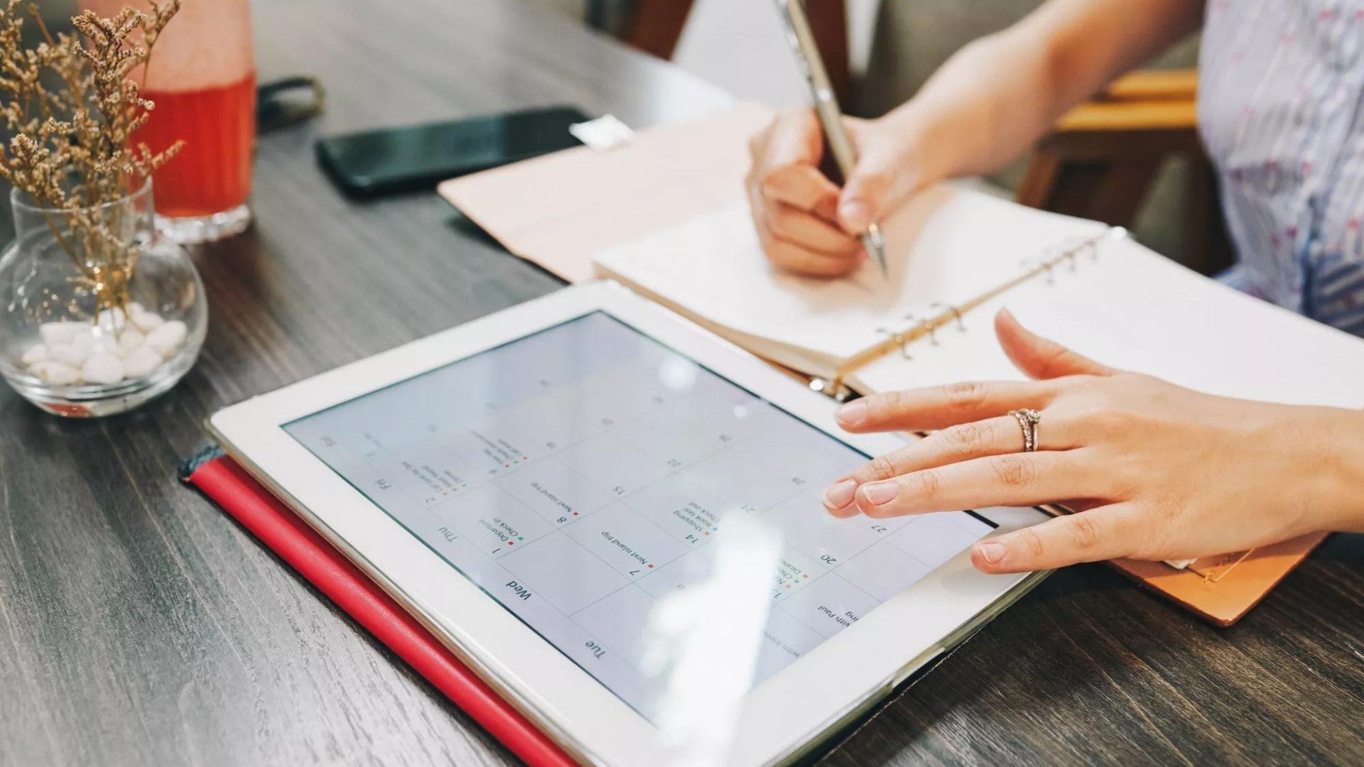 Person adding financial dates to paper calendar and computer calendar.