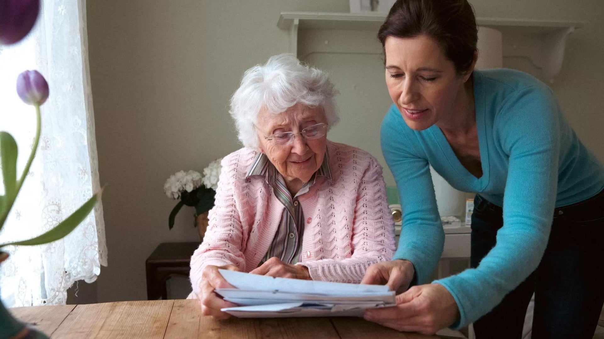 Woman reading to her mother at the table.