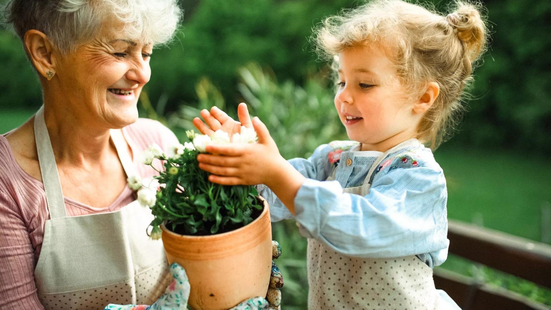 Senior grandmother with young granddaughter gardening on a balcony in the summer.