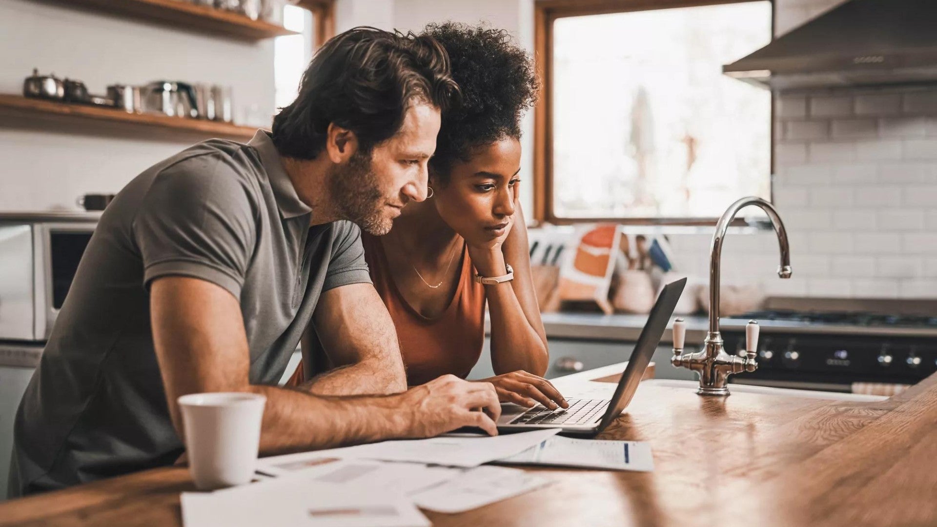 Couple in their kitchen doing financial planning on a laptop.