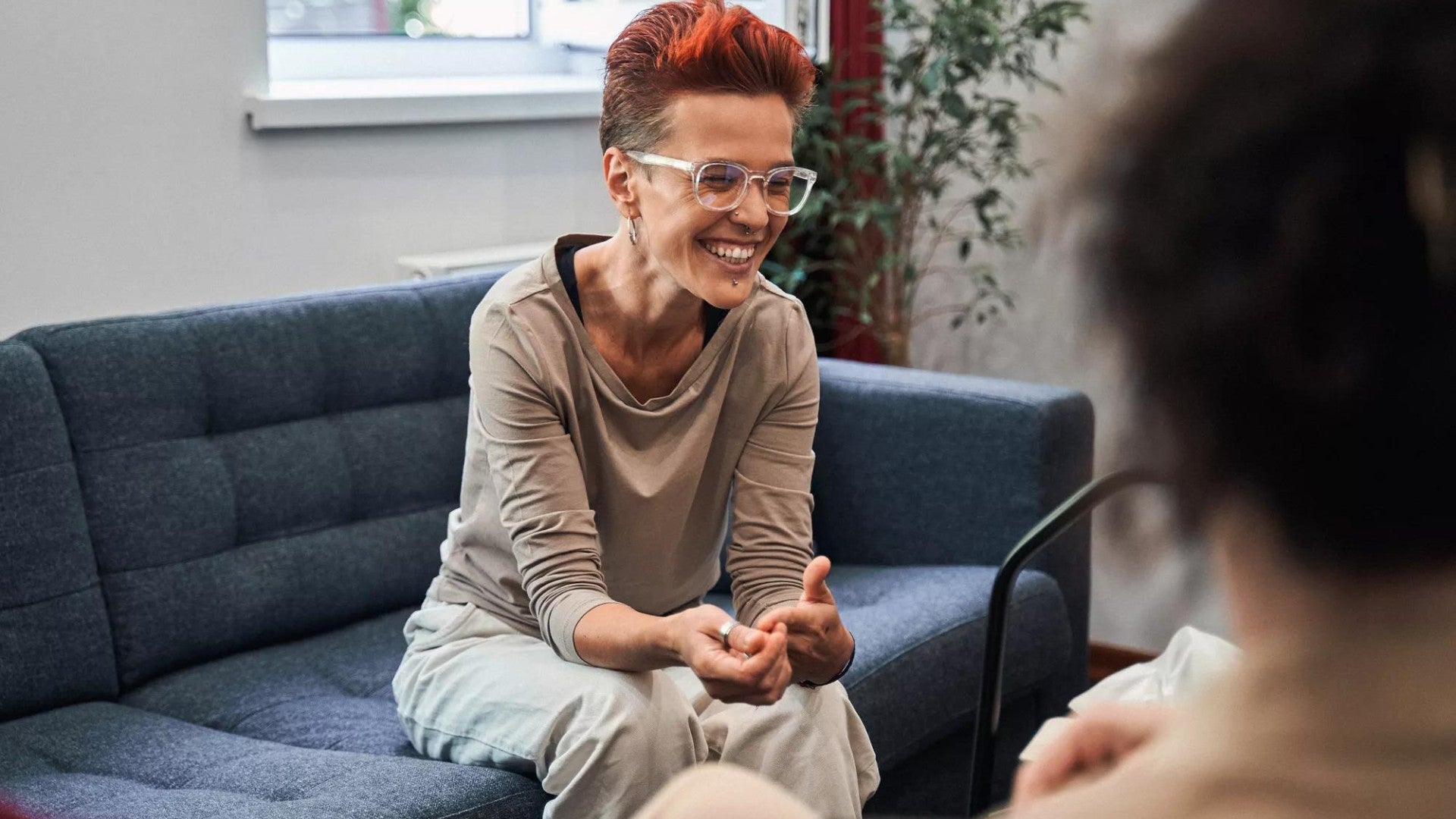 Woman laughing out loud while sitting at sofa and talking with her doctor during therapy.