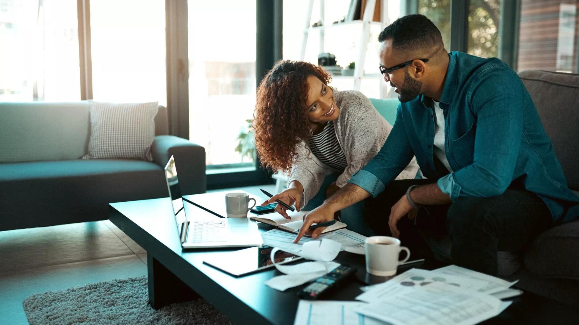 Black couple sitting together on a couch paying bills and reviewing finances