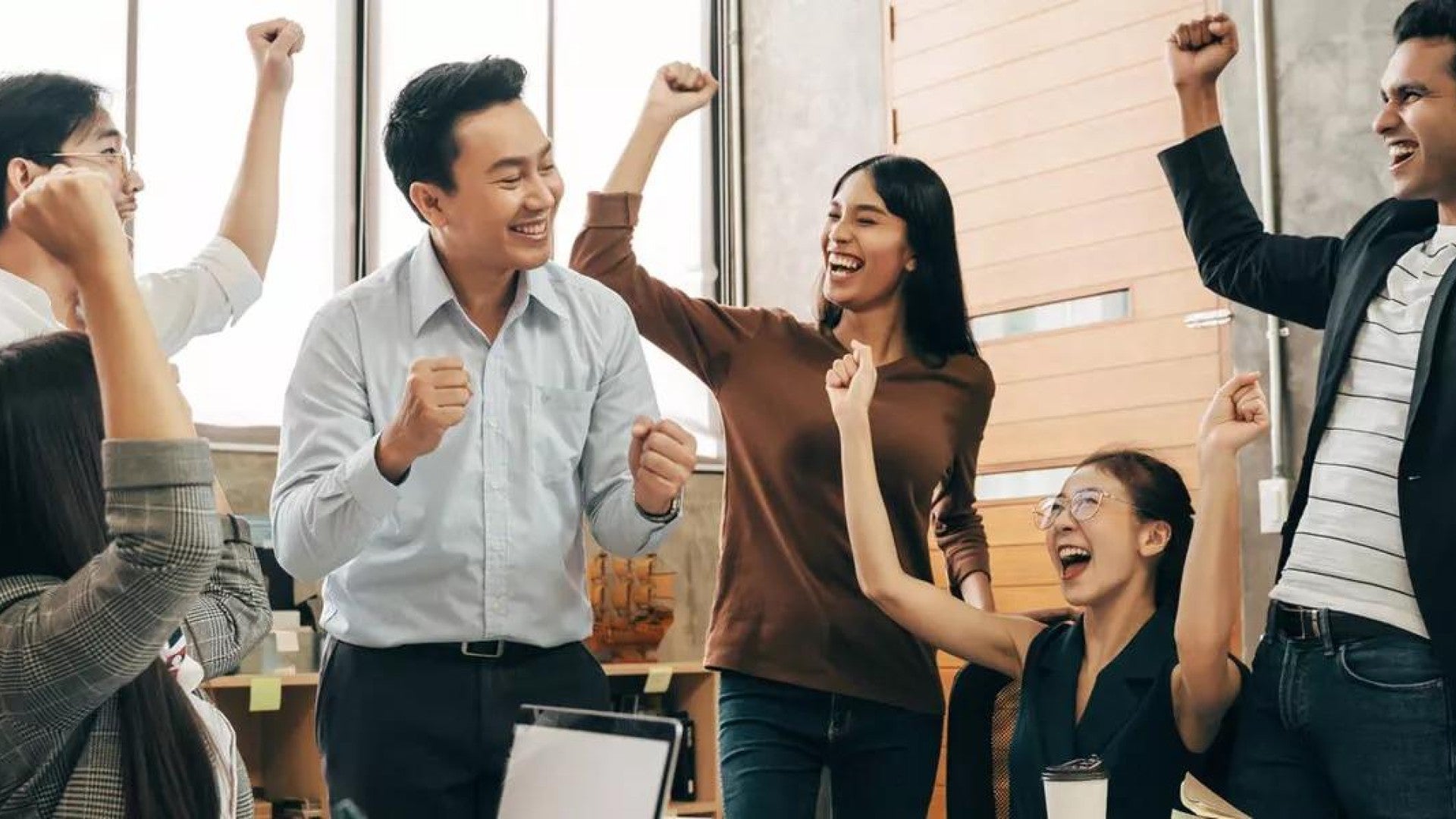 Smiling employees in an office raise their arms in celebration.