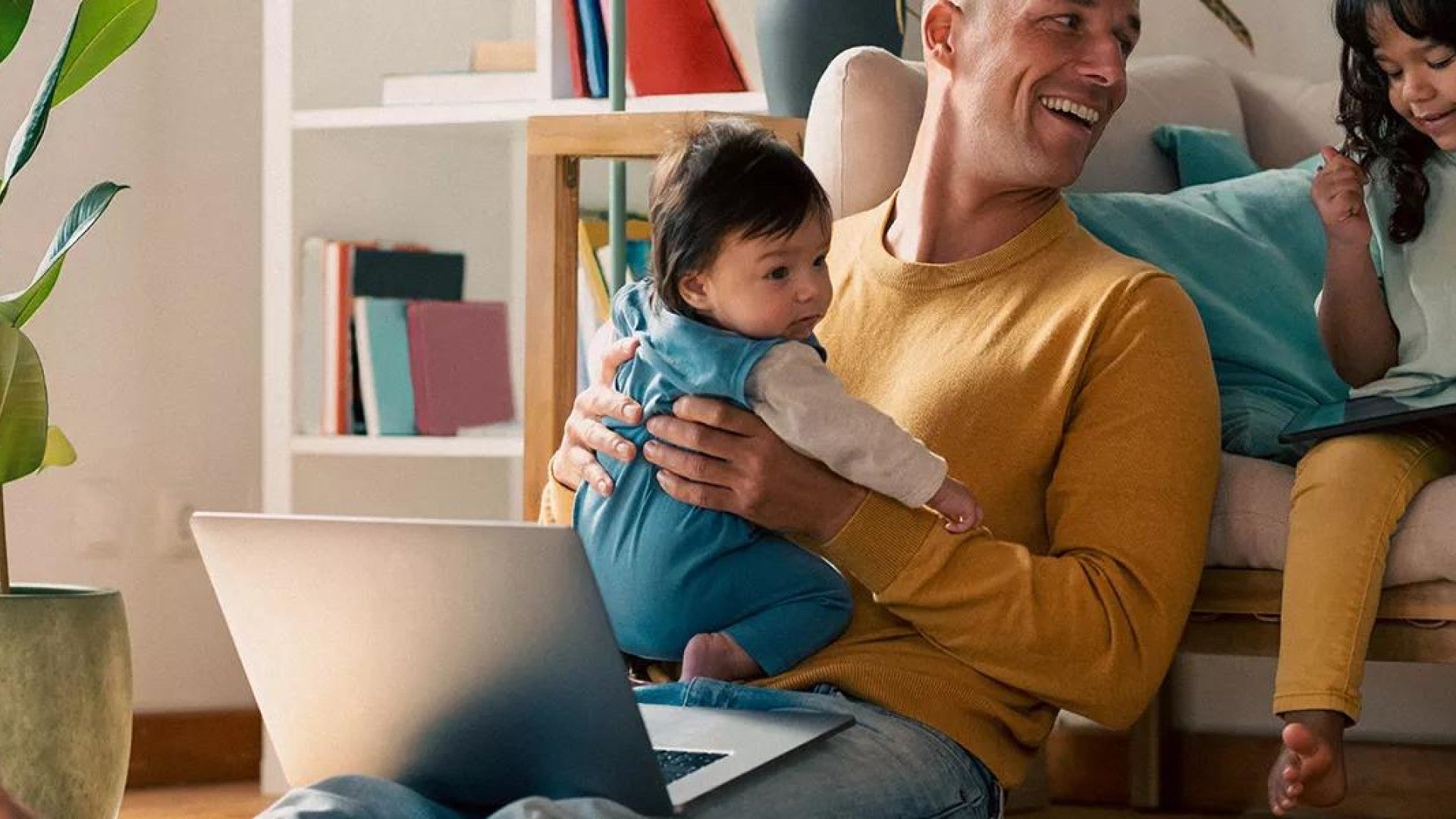 Father holding child and talking to another child while looking at budget on computer