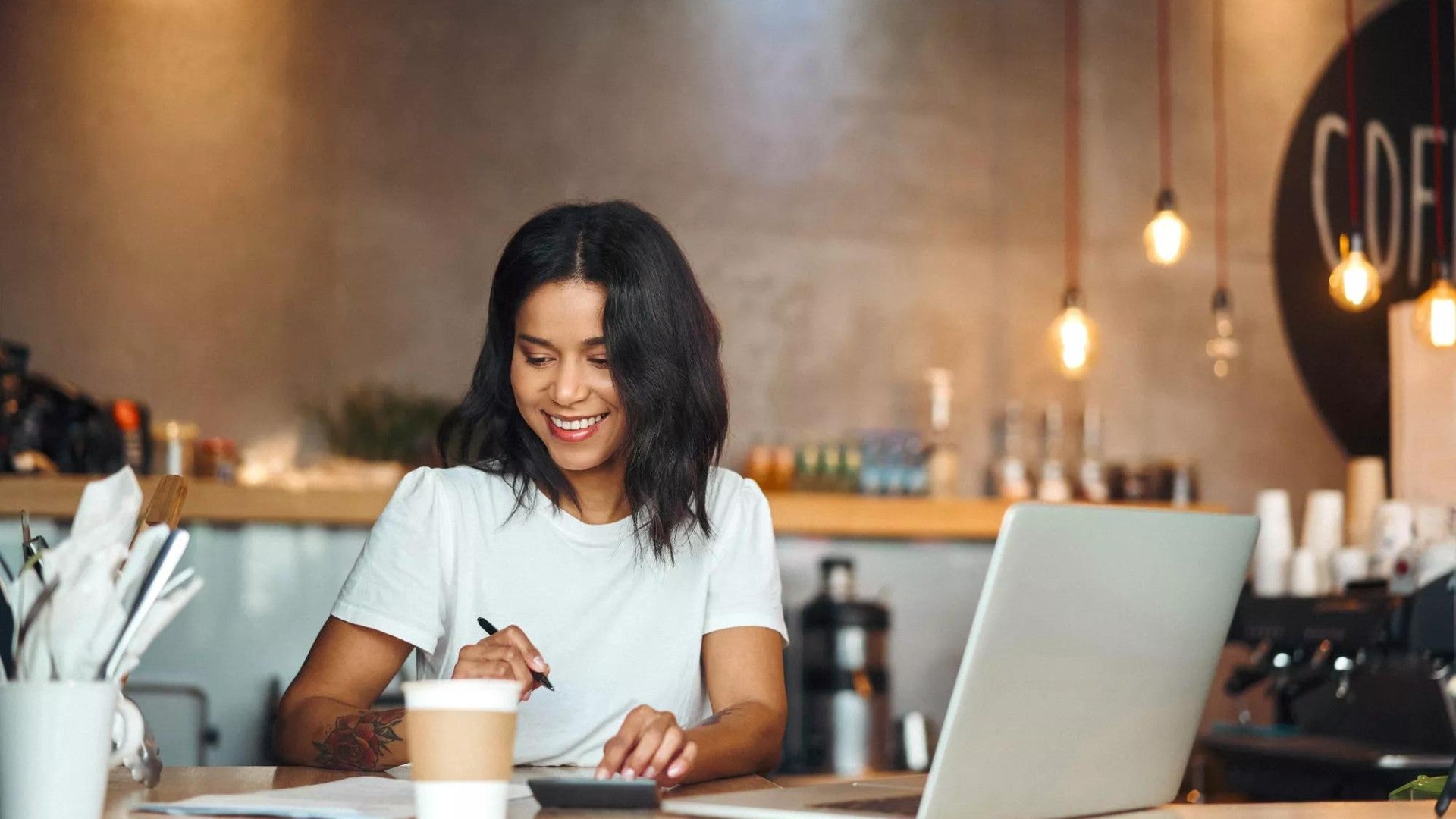 Business owner with coffee and a laptop, smiling as she works.