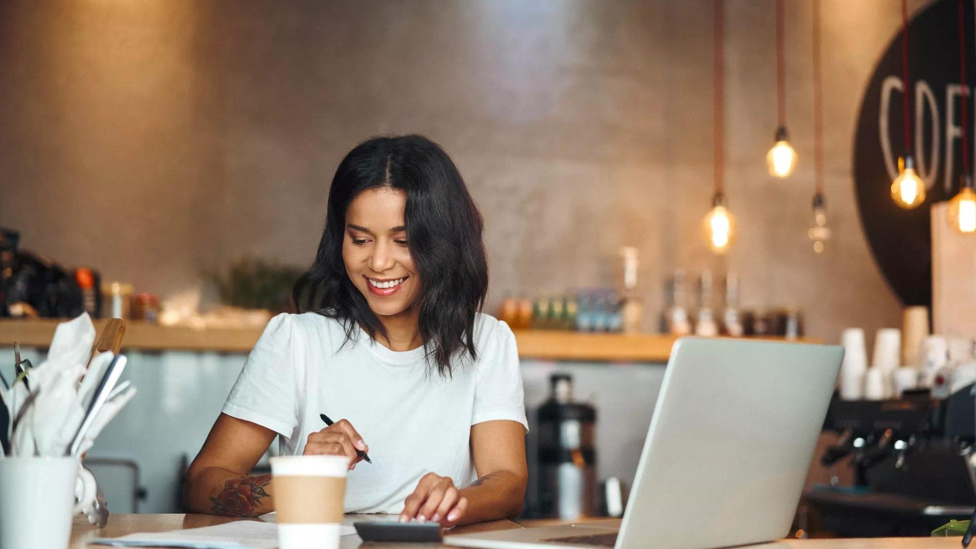 Business owner with coffee and a  laptop, smiling as she works.