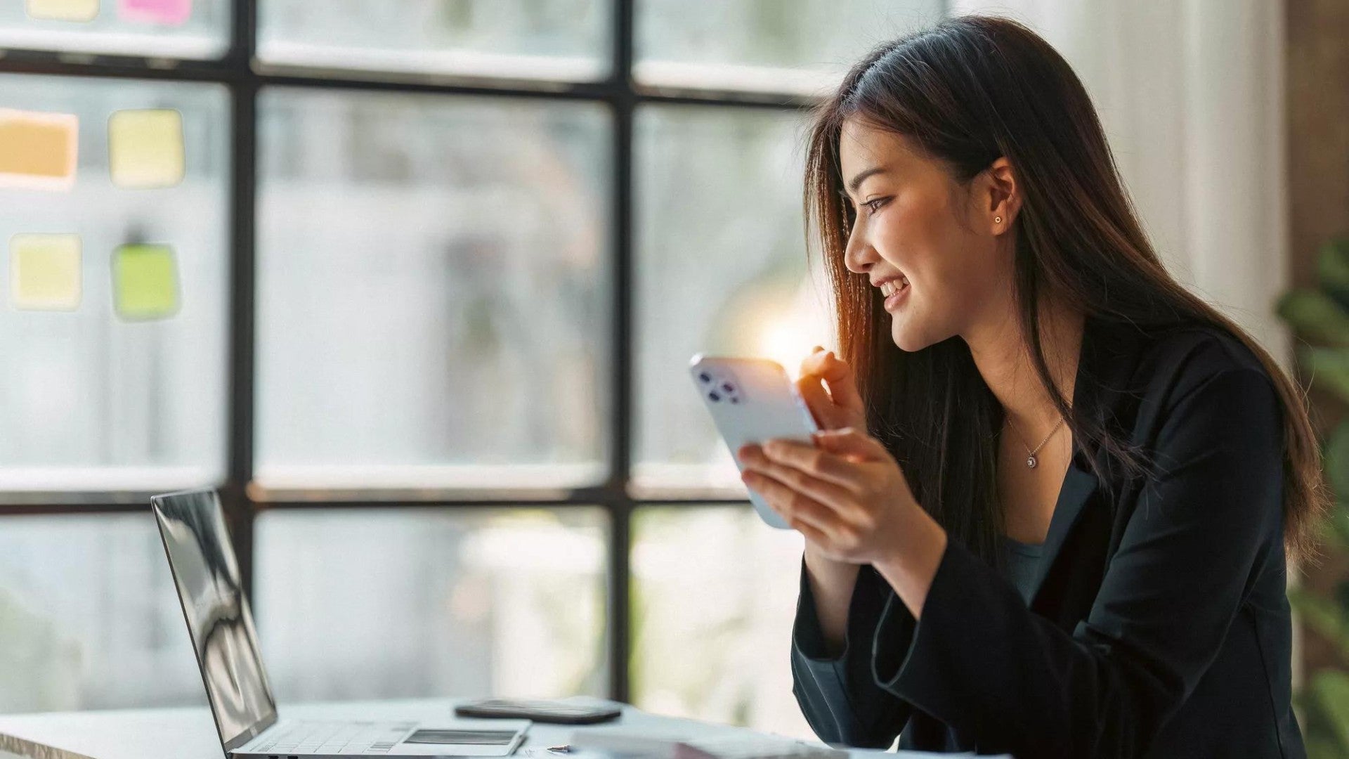 Young woman using her laptop and checking her phone.