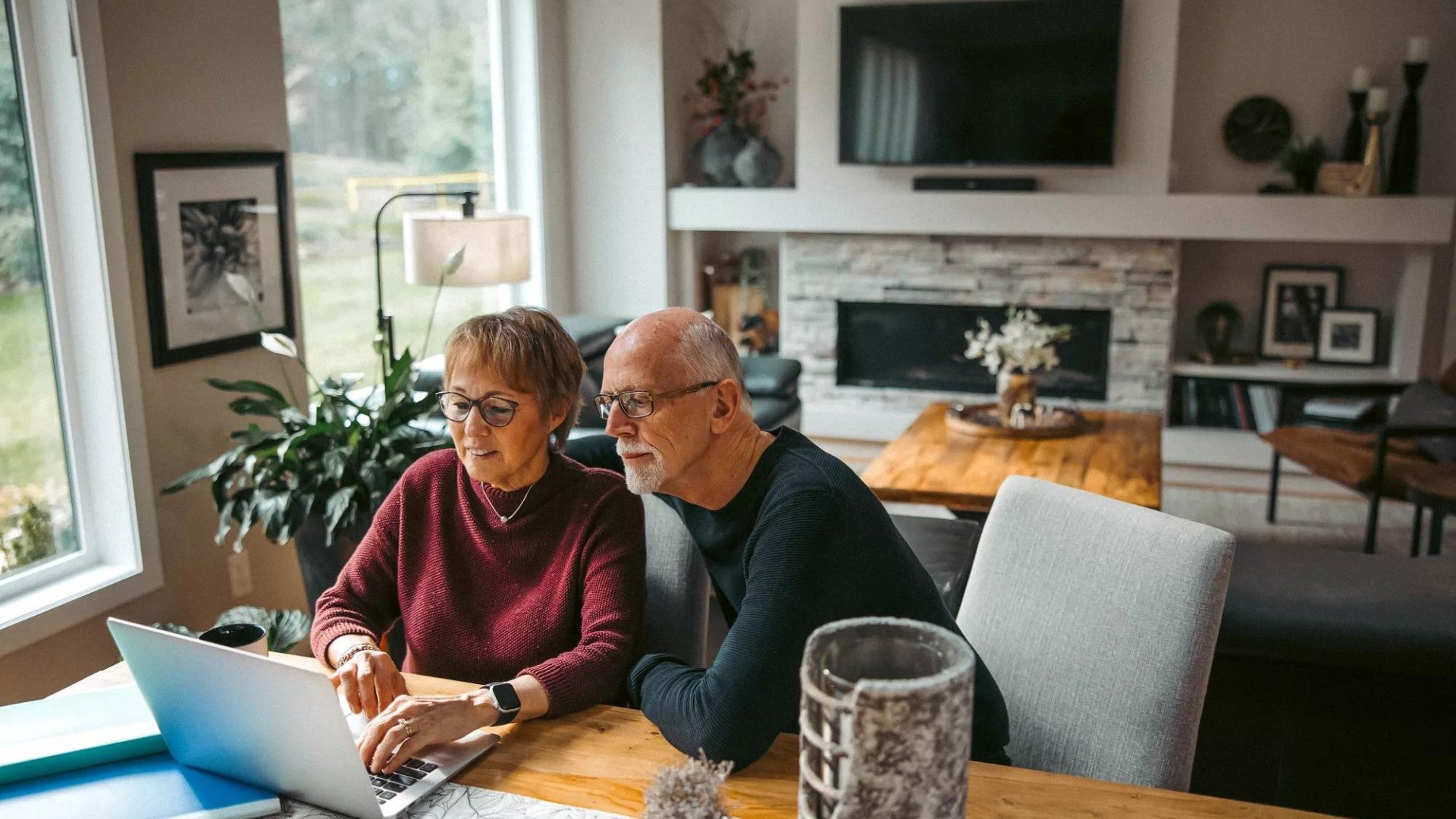 Older couple working together on laptop from dining room table.