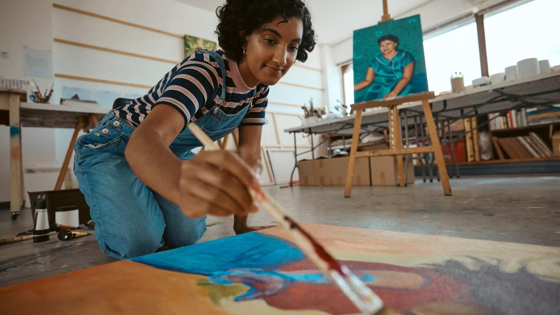 Young adult in art studio holding a paintbrush and getting ready to work on a large painting canvas