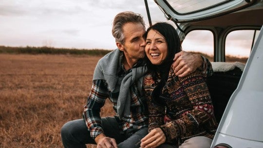 Middle aged couple sitting on the trunk of a car.