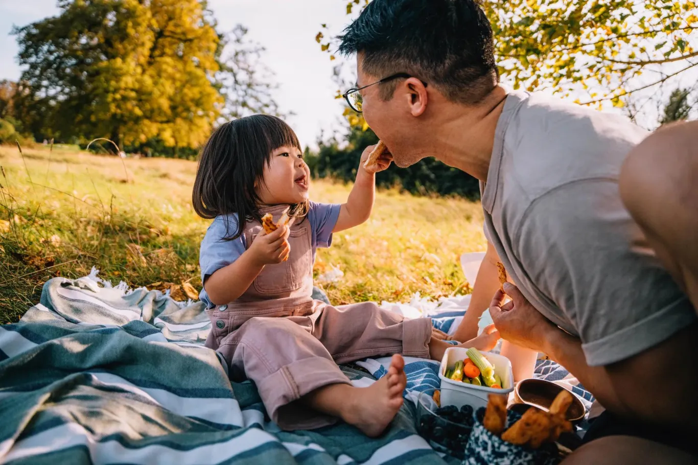 Father and daughter sitting on blanket outside having a picnic.
