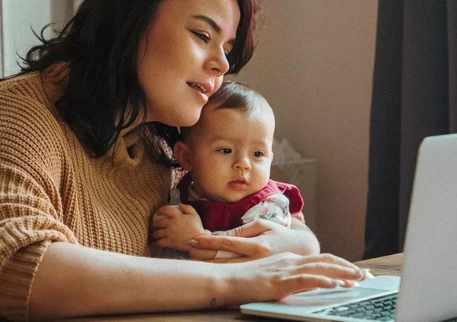 Woman holding a baby on her lap while she looks at her credit score on a computer